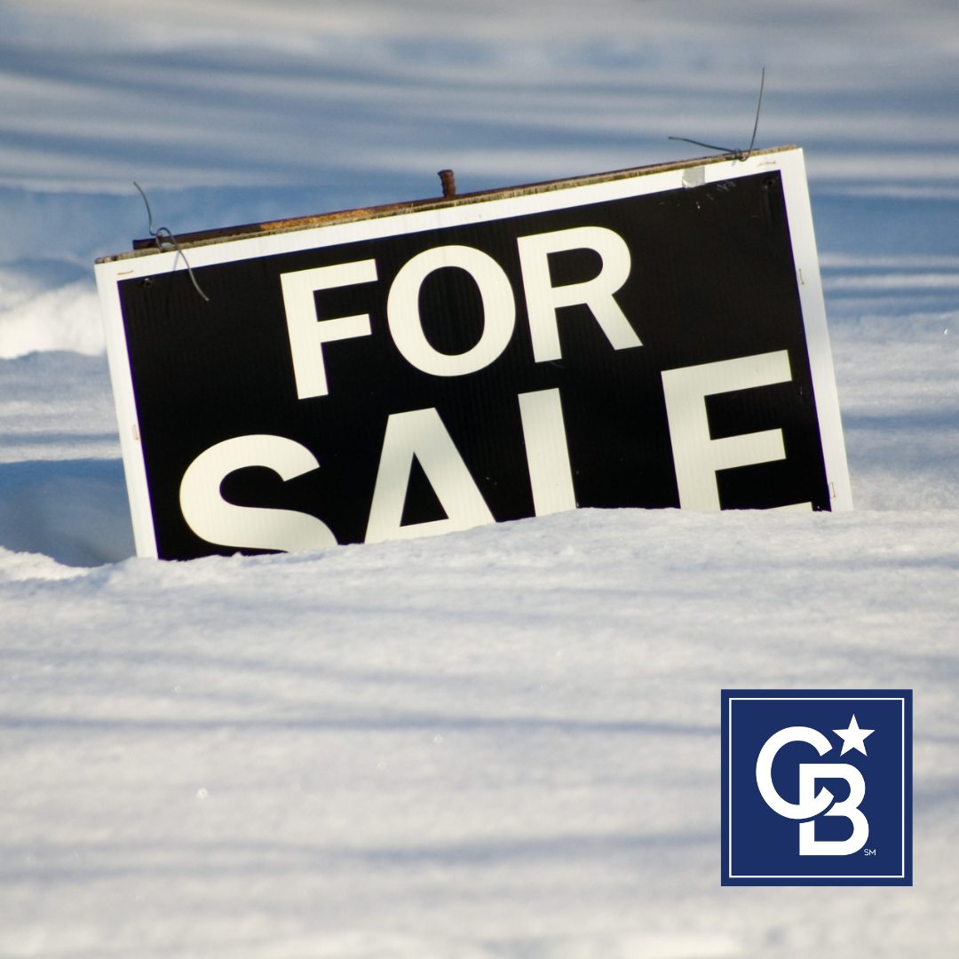 A "For Sale" sign partially covered in snow, advantages of buying a home in winter