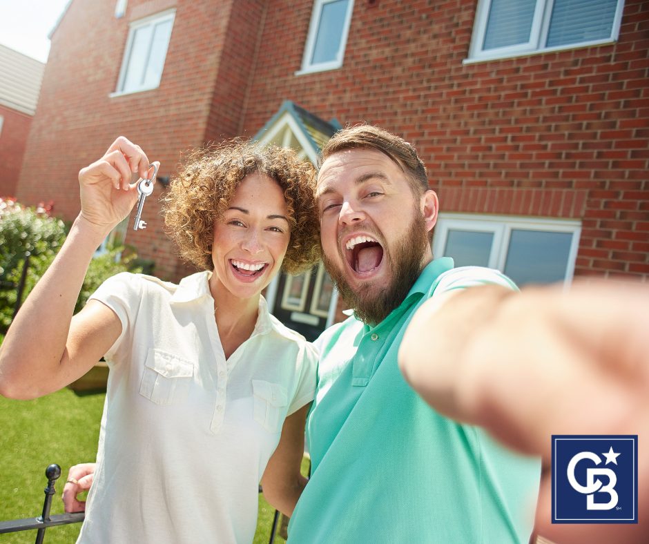 A happy couple taking a selfie in front of their new home, celebrating their purchase as more buyers re-enter the market.