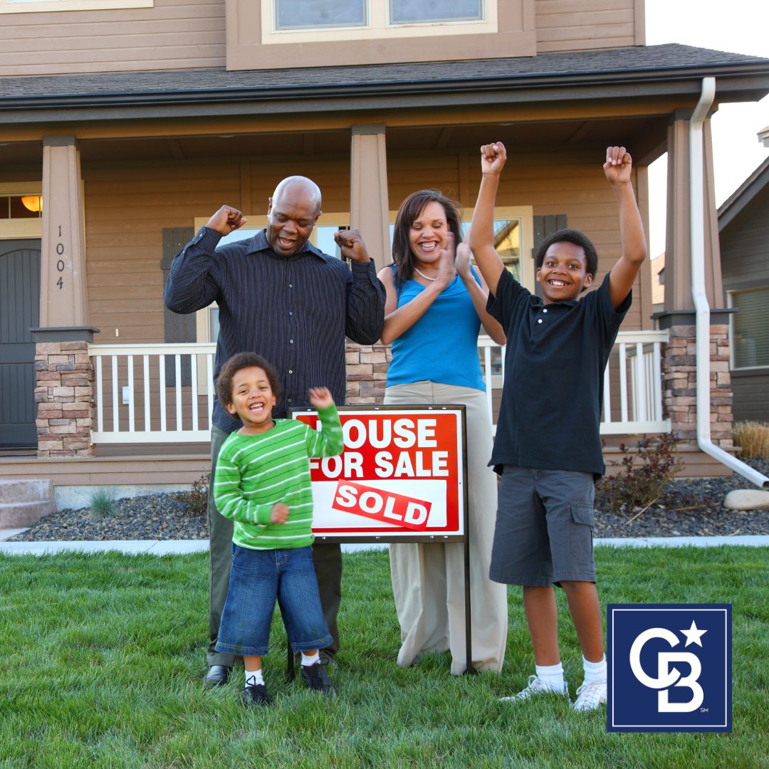 Happy family celebrating in front of their new home with a “SOLD” sign, representing the best time to buy a home.