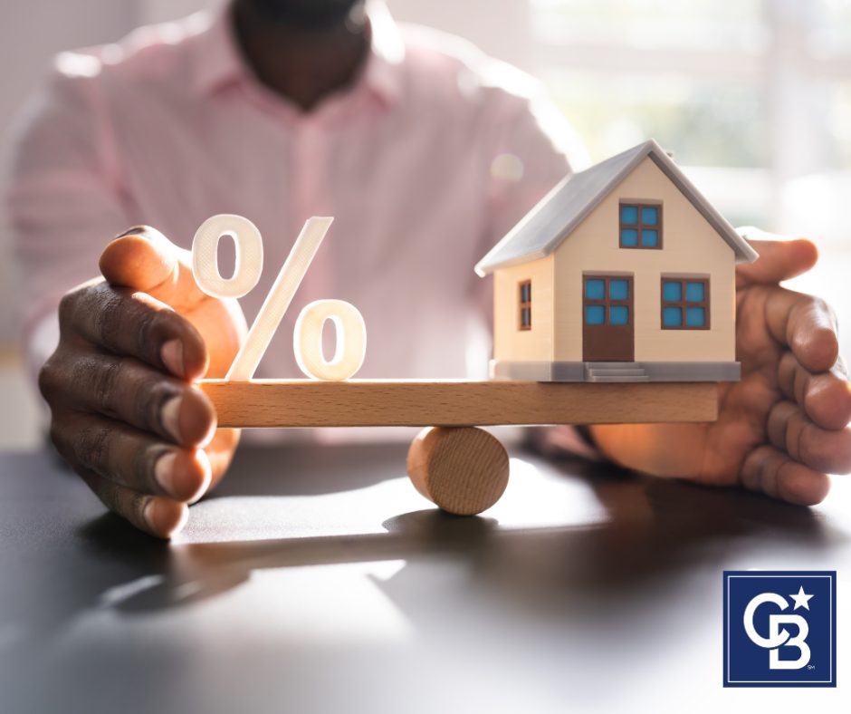 A man balances a scale with a percent sign on one side and a house on the other, symbolizing mortgage rates in Denver and housing affordability.
