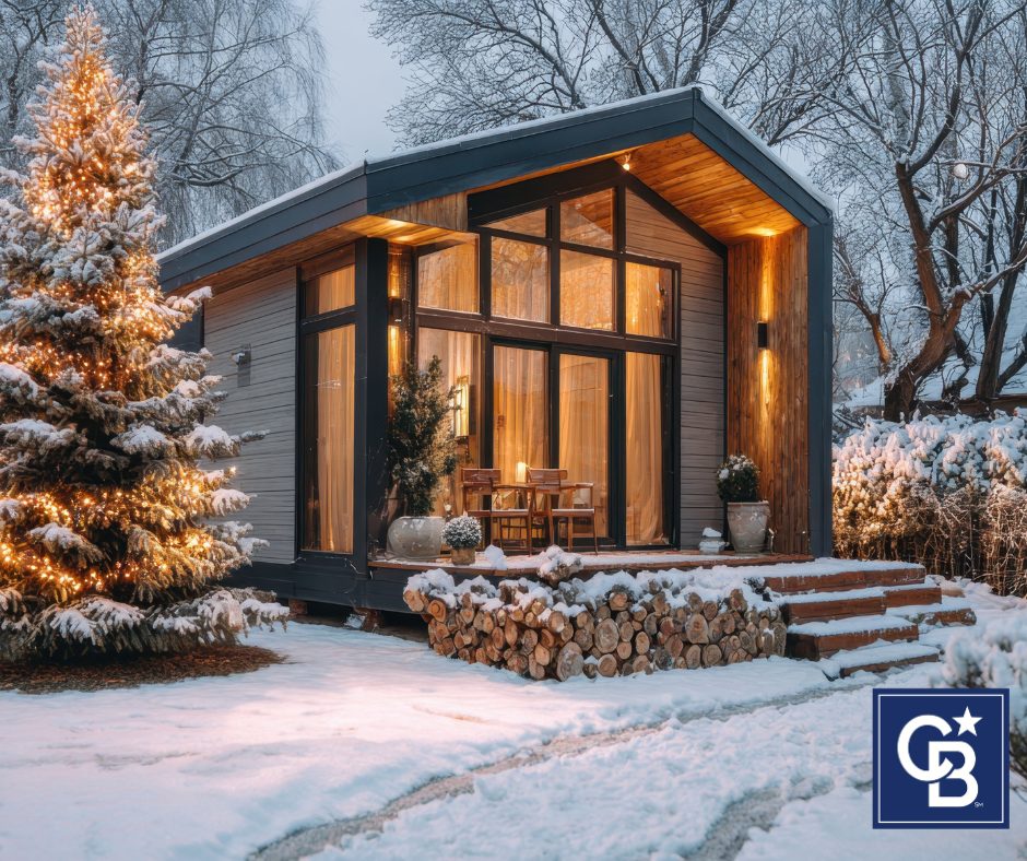 Warm, inviting front of a house in winter with snow on the ground, a lit tree by the entryway, and soft golden lights glowing from the windows, showing how to get your home ready for a winter sale.